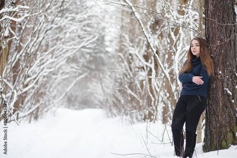 A young girl in a winter park on a walk. Christmas holidays in the winter forest. The girl enjoys winter in the park.