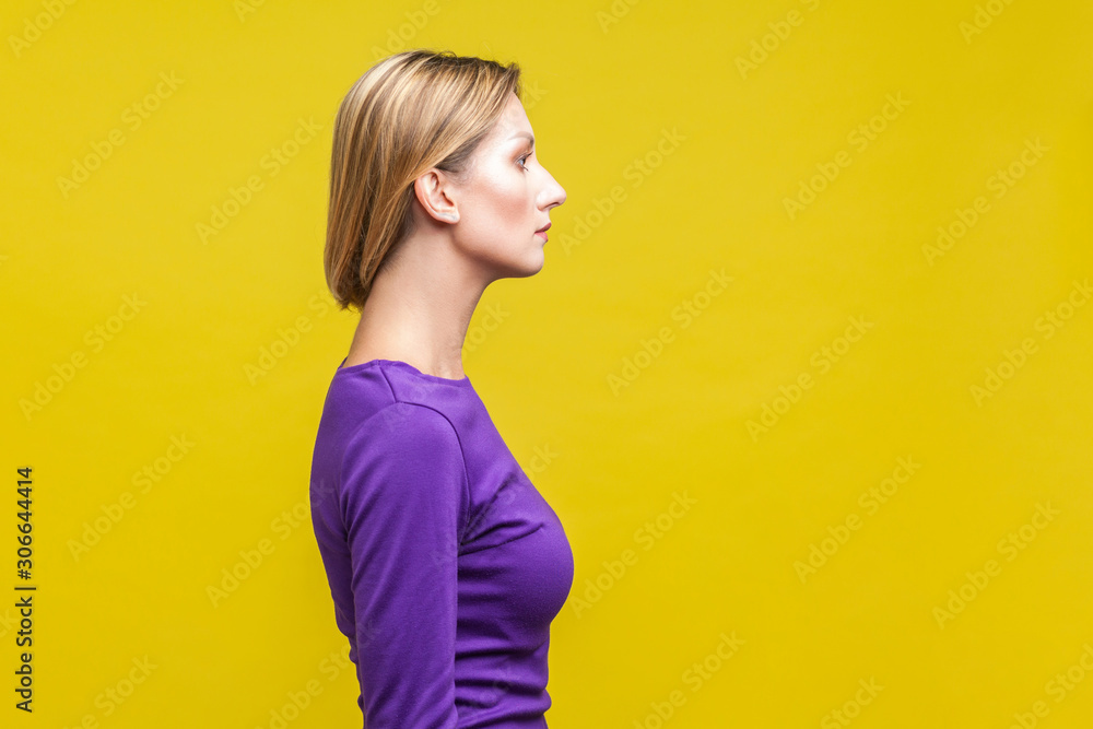 Side view of beautiful serious woman in elegant purple dress showing her neck with clean young skin, beauty skincare concept, copy space on right side. indoor studio shot isolated on yellow background Side view of beautiful serious woman in elegant purple dress showing her neck with clean young skin, beauty skincare concept, copy space on right side. indoor studio shot isolated on yellow background