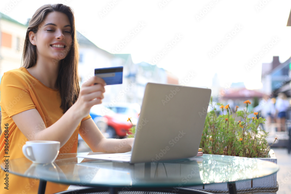 Happy natural brunette using credit card and laptop in cafe outdoors. Happy natural brunette using credit card and laptop in cafe outdoors.