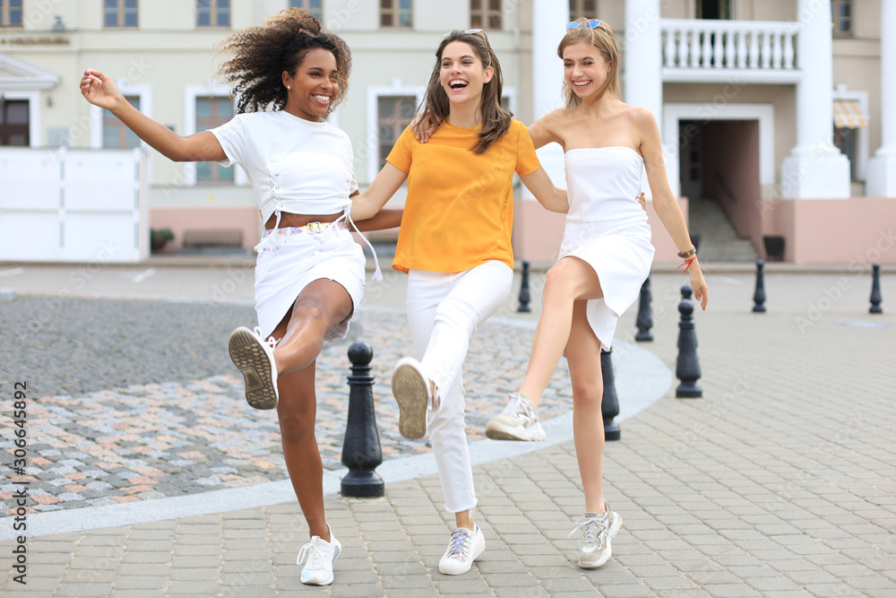 Three young smiling hipster women in summer clothes posing on street.Female showing positive face emotions. Dancing. Three young smiling hipster women in summer clothes posing on street.Female showing positive face emotions. Dancing.