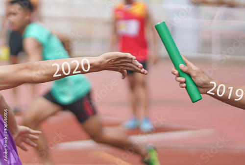 Professional Athlete passing a baton to the partner against race on racetrack.between 2019 and 2020 years.happy new year 2020.