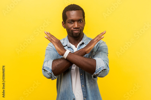 Never again. Portrait of absolutely convinced man in denim casual shirt standing crossing hands, showing x sign meaning stop, there is no way, finish. indoor studio shot isolated on yellow background