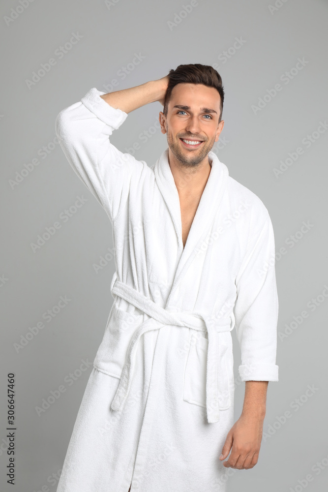 Happy young man in bathrobe on light grey background