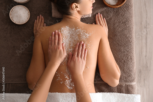 Young woman having body scrubbing procedure with sea salt in spa salon, top view