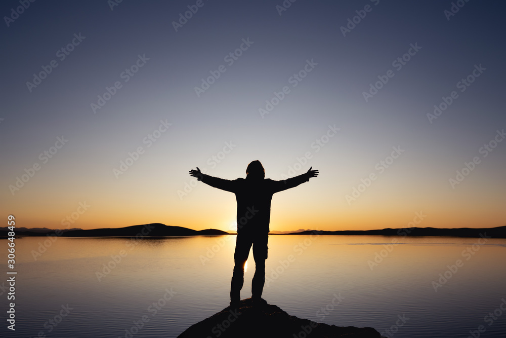 Silhouette with raised arms against sunset lake