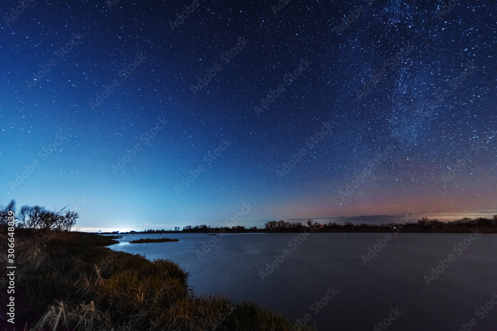 A magical starry night on the river bank with a milky way in the sky and falling stars in the winter.