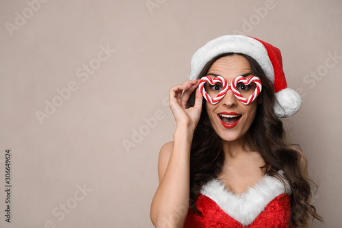 Emotional woman in Christmas costume with party glasses on beige background  space for text