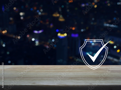Security shield with check mark flat icon on wooden table over blur colorful night light modern city tower and skyscraper, Technology internet cyber security and anti virus concept © grapestock