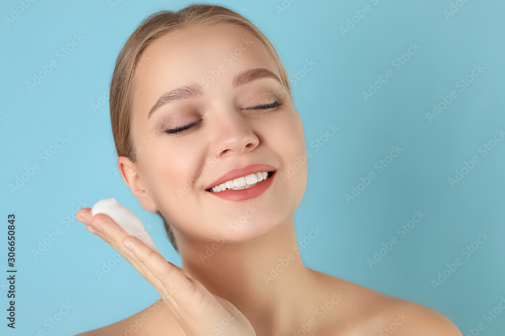 Young woman washing face with cleansing foam on light blue background. Cosmetic product Young woman washing face with cleansing foam on light blue background. Cosmetic product