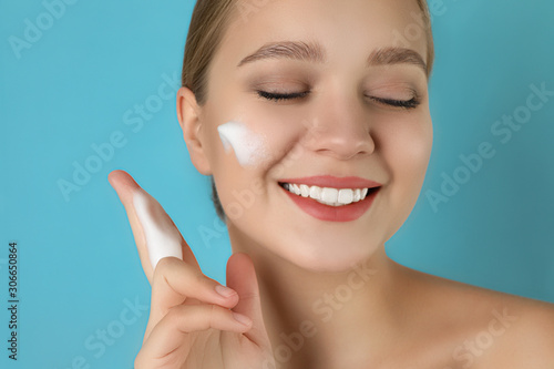 Young woman washing face with cleansing foam on light blue background. Cosmetic product