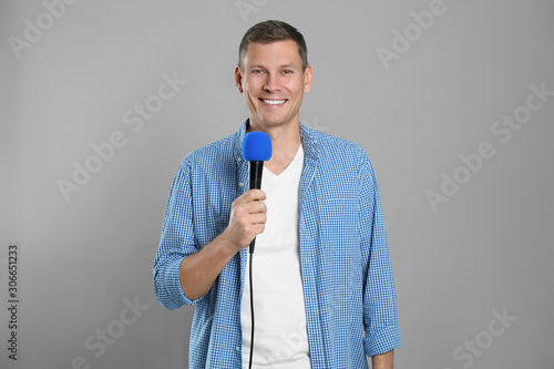 Male journalist with microphone on grey background