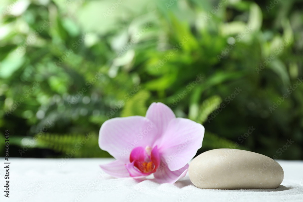Stone and beautiful flower on sand against blurred green background. Zen, meditation, harmony Stone and beautiful flower on sand against blurred green background. Zen, meditation, harmony