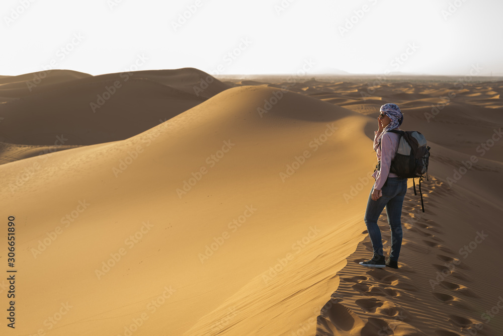 Woman with turban watching the dune landscape in the Sahara desert.