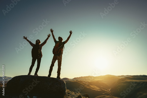 Two happy hikers stands against sunset