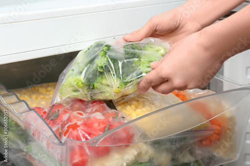 Schilderij op canvas Woman putting plastic bag with broccoli in refrigerator with frozen vegetables,