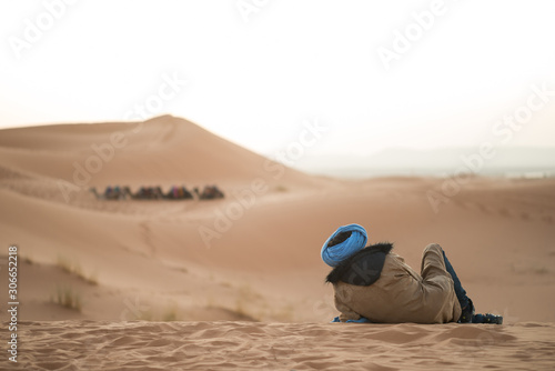 Berber man watching a group of dromedary camels in the dunes of the Sahara desert. © ROM