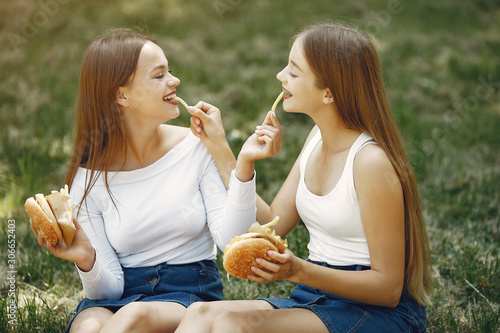 Beautiful girls in a jeans skirts. Women in a summer park. Friends with a burgers