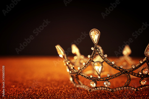 low key image of beautiful queen/king crown over gold glitter table. vintage filtered. fantasy medieval period