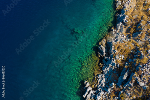 Aerial top view of sea waves hitting rocks on the beach with turquoise sea water. Amazing rock cliff seascape in Greece coastline. Drone shot.