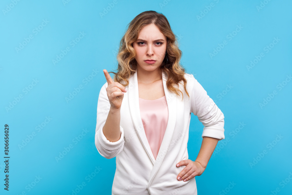 I told you! Portrait of bossy woman with wavy hair in white jacket frowning face and pointing finger up in warning gesture, teacher scolding with displeased expression. studio shot, blue background I told you! Portrait of bossy woman with wavy hair in white jacket frowning face and pointing finger up in warning gesture, teacher scolding with displeased expression. studio shot, blue background