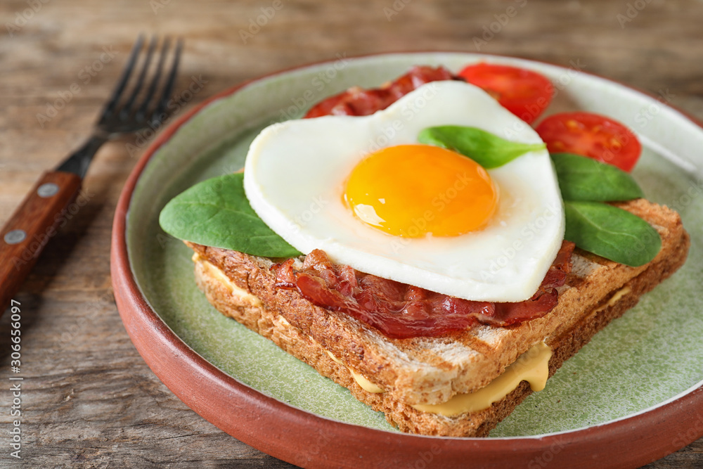 Plate of tasty sandwich with heart shaped fried egg and bacon on wooden table, closeup Plate of tasty sandwich with heart shaped fried egg and bacon on wooden table, closeup