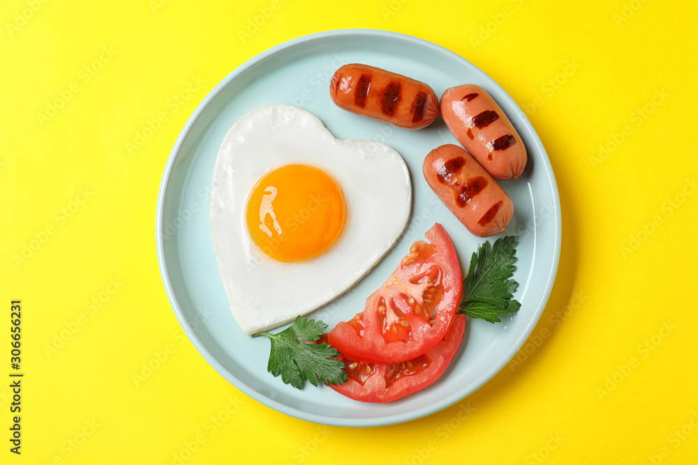 Plate of heart shaped fried egg and sausages on yellow background, top view Plate of heart shaped fried egg and sausages on yellow background, top view