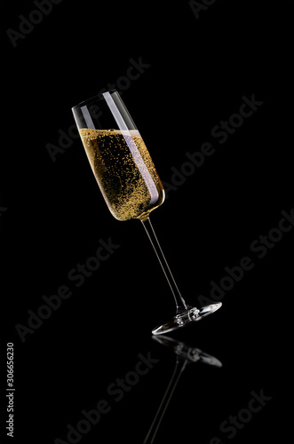 A glass of champagne, without the foam on a dark background is tilted to the left.
