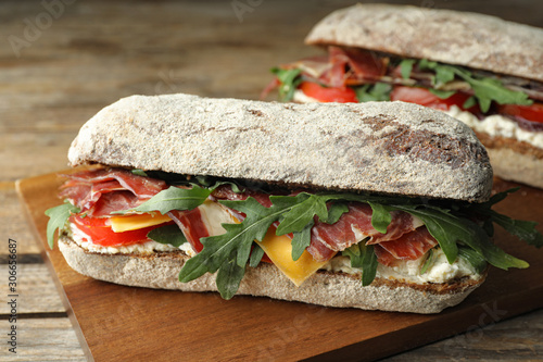 Delicious sandwich with fresh vegetables and prosciutto on wooden table, closeup photo