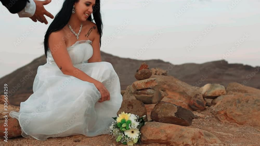 Newlywedded couple Groom destroys Brides beautiful pile of stacked rocks stone balancing structure on their wedding day at remote seaside coastal region destruction slow motion panaromic color graded