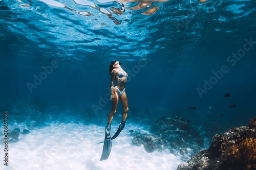 Freediver girl with fins glides over sandy bottom with fishes in blue ocean photo