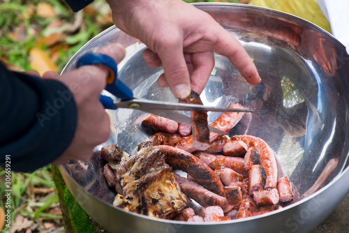 man cutting sausages and barbecue meat in a metal bowl