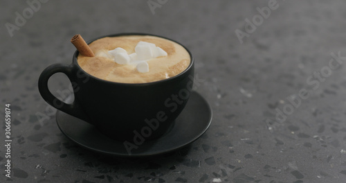 cappuccino with marshmallow and cinnamon in black cup on terrazzo countertop