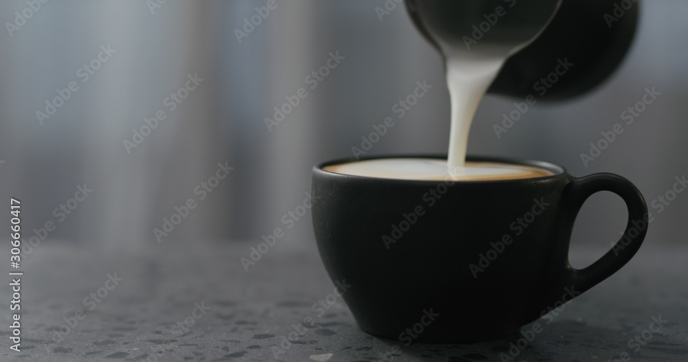 pouring steamed milk into cappuccino in black cup on terrazzo countertop pouring steamed milk into cappuccino in black cup on terrazzo countertop