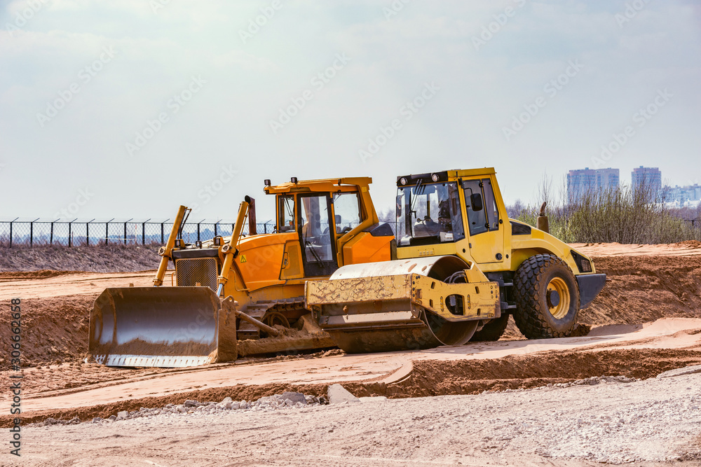 Obraz premium Road roller and bulldozer stand on sand surface during the new road construction process.