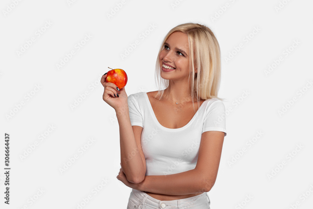 Beautiful, sexy blonde girl with perfect healthy hair and natural make-up smiling in the studio with an apple, portrait of a young woman on a white background Beautiful, sexy blonde girl with perfect healthy hair and natural make-up smiling in the studio with an apple, portrait of a young woman on a white background