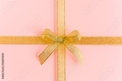 Gold ribbon with bow, isolated on pink background. Colorful celebration, birthday background. Flat lay, top view