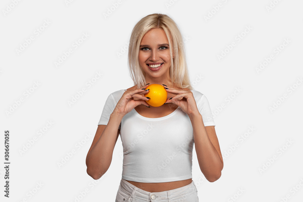 Beauty, sexy blonde girl with perfect healthy hair and natural makeup posing in studio with an orange. Young woman portrait isolated on white background Beauty, sexy blonde girl with perfect healthy hair and natural makeup posing in studio with an orange. Young woman portrait isolated on white background