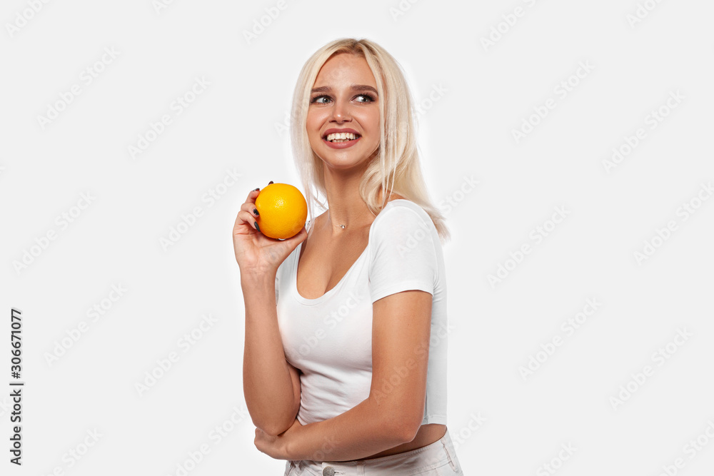 Beauty, sexy blonde girl with perfect healthy hair and natural makeup posing in studio with an orange. Young woman portrait isolated on white background Beauty, sexy blonde girl with perfect healthy hair and natural makeup posing in studio with an orange. Young woman portrait isolated on white background