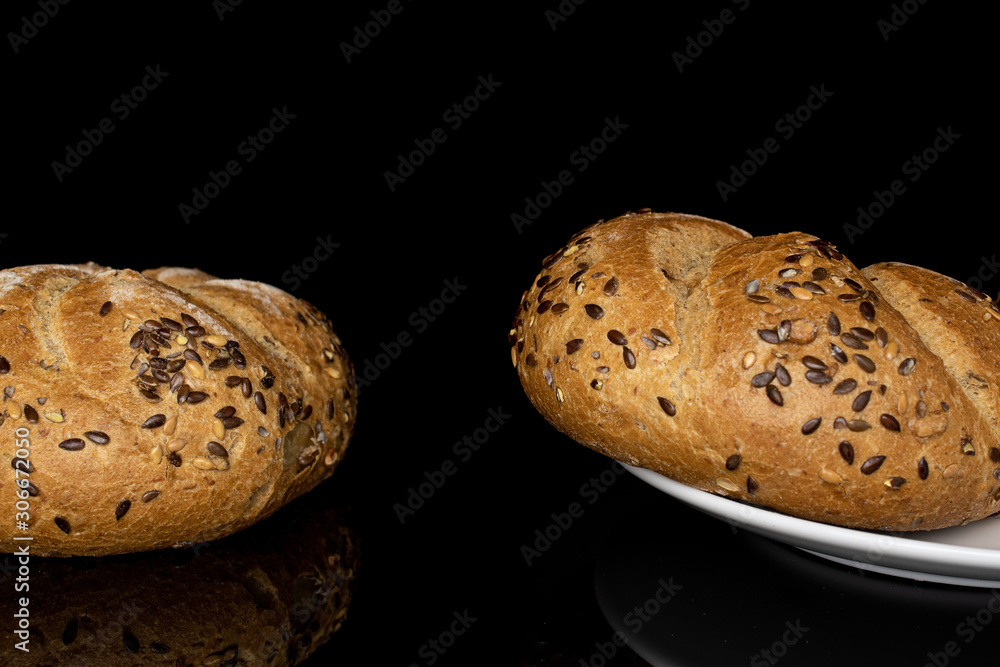 Group of two whole sesame kaiser roll on white ceramic plate isolated on black glass