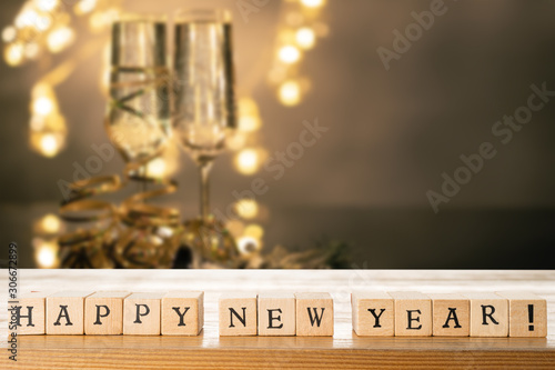 Obraz na płótnie Happy New Year text made out of wooden blocks. Two glasses of champane with festive new year's eve decoration in the background. Copy space in the top right corner. w salonie