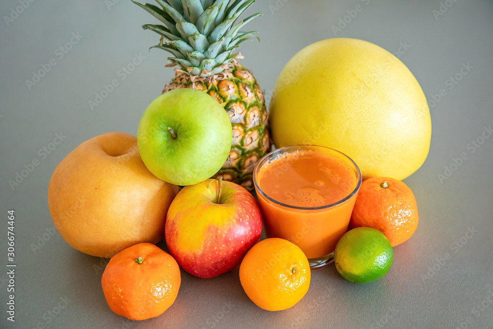 Different tropical fruits and orange smoothie on grey background, healthy eating lifestyle concept Different tropical fruits and orange smoothie on grey background, healthy eating lifestyle concept