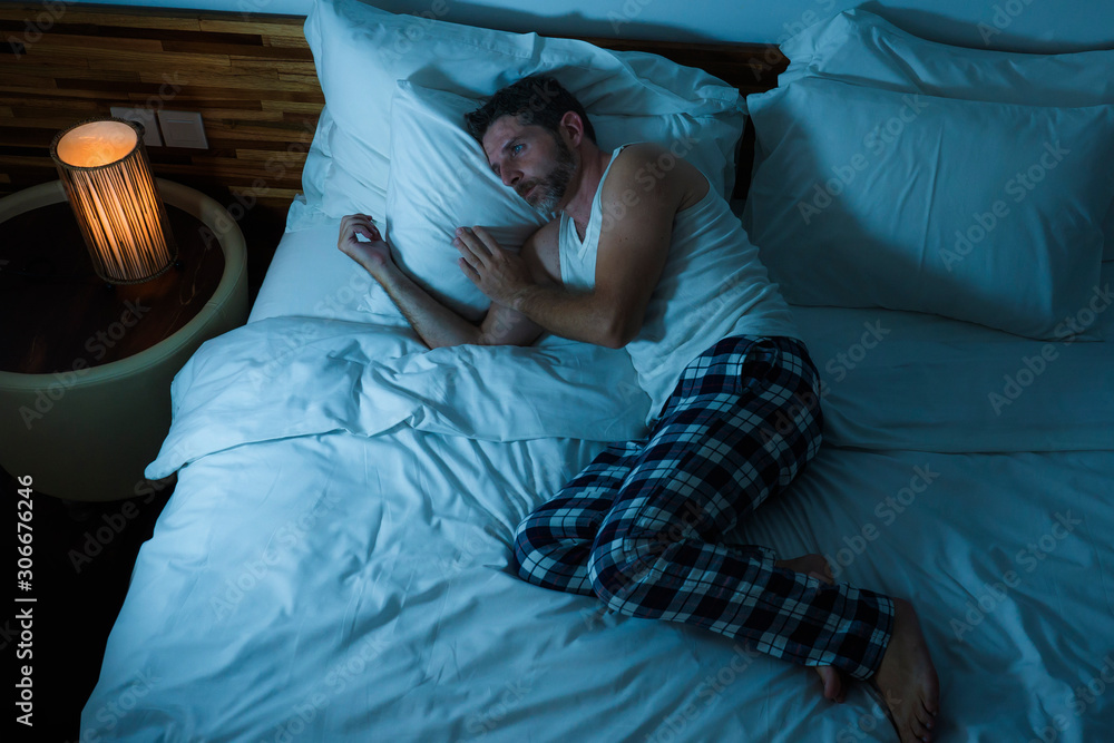 dramatic lifestyle portrait of young attractive sad and depressed man lying  on bed at night feeling stressed and desperate suffering depression problem  in sadness and pain Stock Photo | Adobe Stock