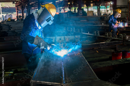 The welder is welding a steel structure work with process Flux Cored Arc Welding(FCAW) and dressed properly with personal protective equipment(PPE) for safety, at industrial factory. © Thaweesak