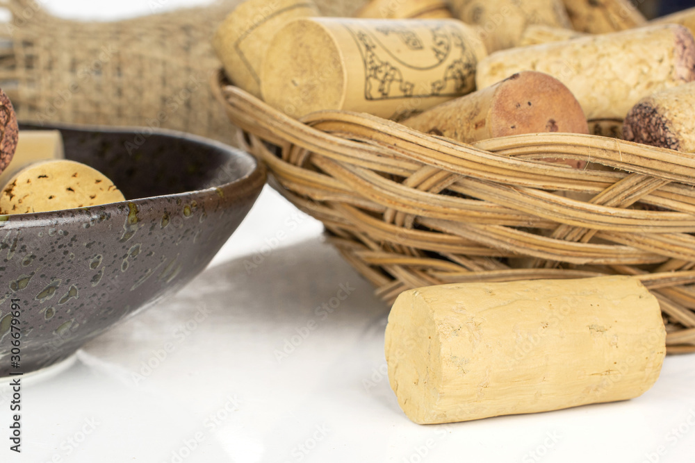 Lot of whole common wine cork  with glass bottle with jute fabric in glazed bowl in round rattan bowl isolated on white background