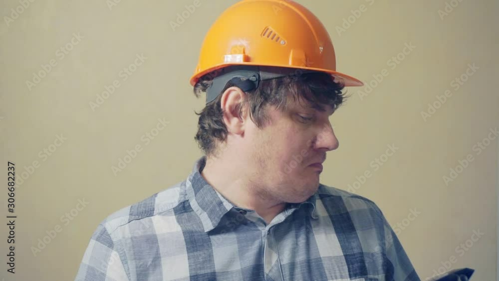 Emotional funny man in a construction helmet with astonishment looks in the documents folder.humorous video portrait of a builder at work Emotional funny man in a construction helmet with astonishment looks in the documents folder.humorous video portrait of a builder at work