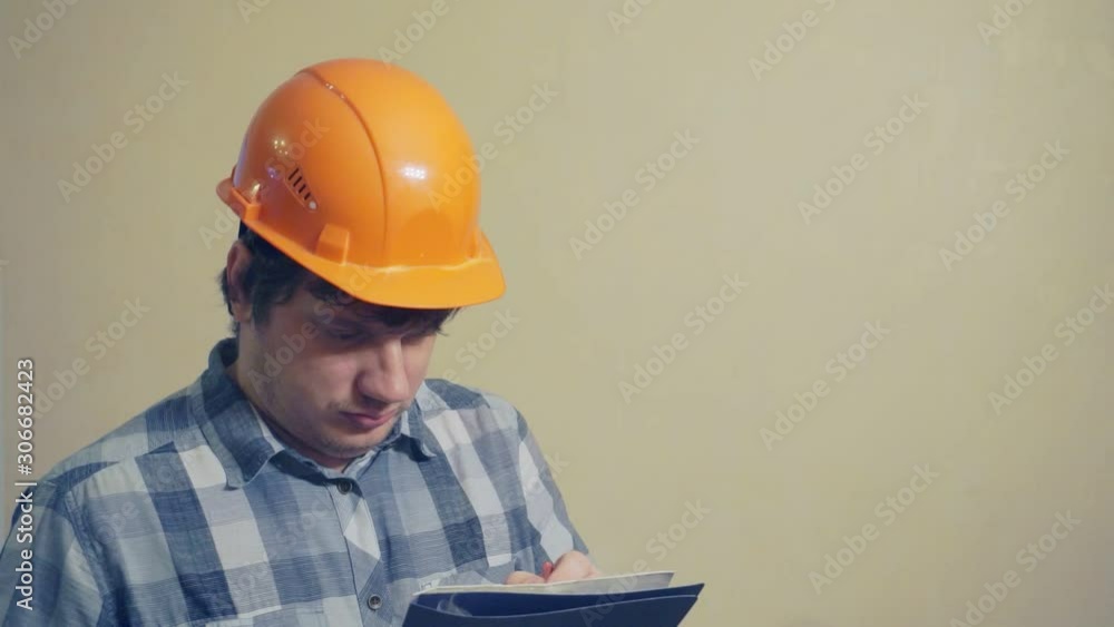 Emotional funny man in a construction helmet with astonishment looks in the documents folder.humorous video portrait of a builder at work Emotional funny man in a construction helmet with astonishment looks in the documents folder.humorous video portrait of a builder at work