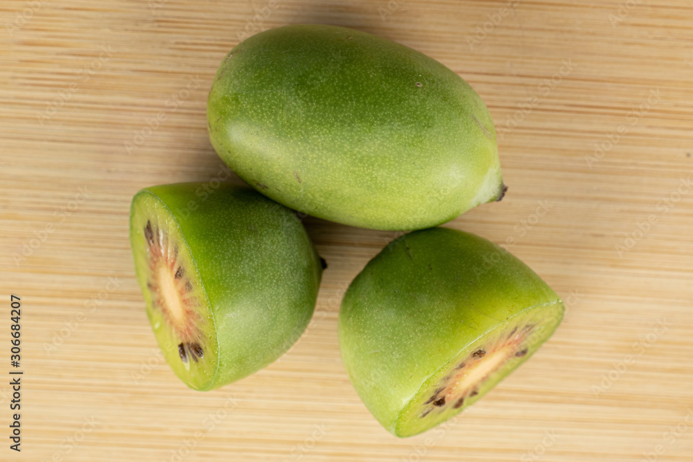 Group of one whole two halves of hardy green kiwi flatlay on light wood