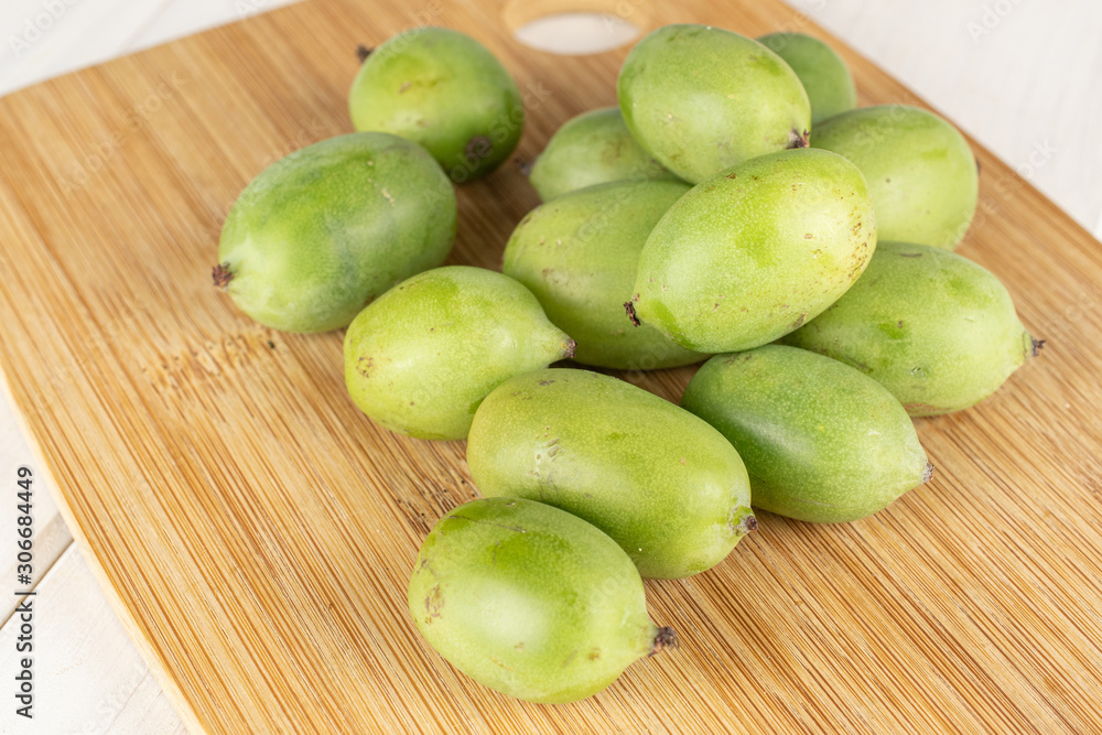 Lot of whole hardy green kiwi on bamboo cutting board on white wood Lot of whole hardy green kiwi on bamboo cutting board on white wood