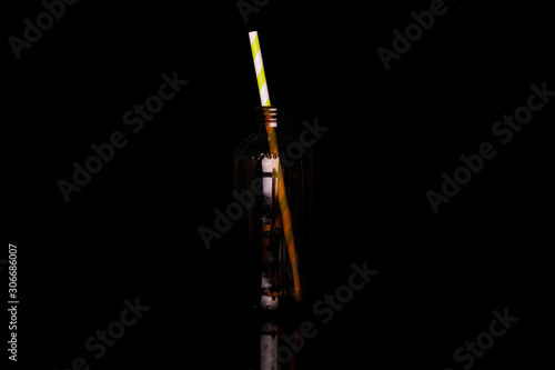 One whole paper straw in brown glass bottle isolated on black glass