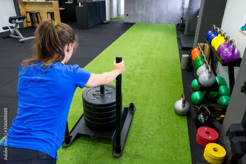 Obraz na płótnie Young female fitness trainer performing sled push in local gym. w salonie